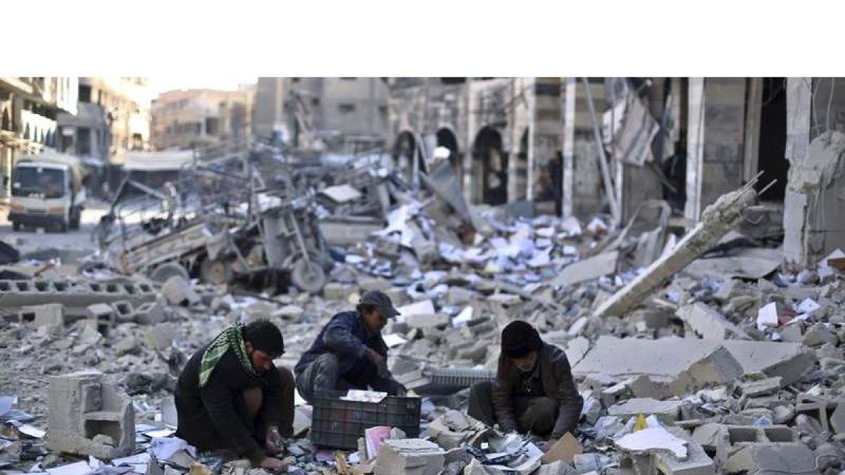Varios hombres recogen objetos entre los escombros tras un bombardeo entre el Daesh y la coalición internacional.