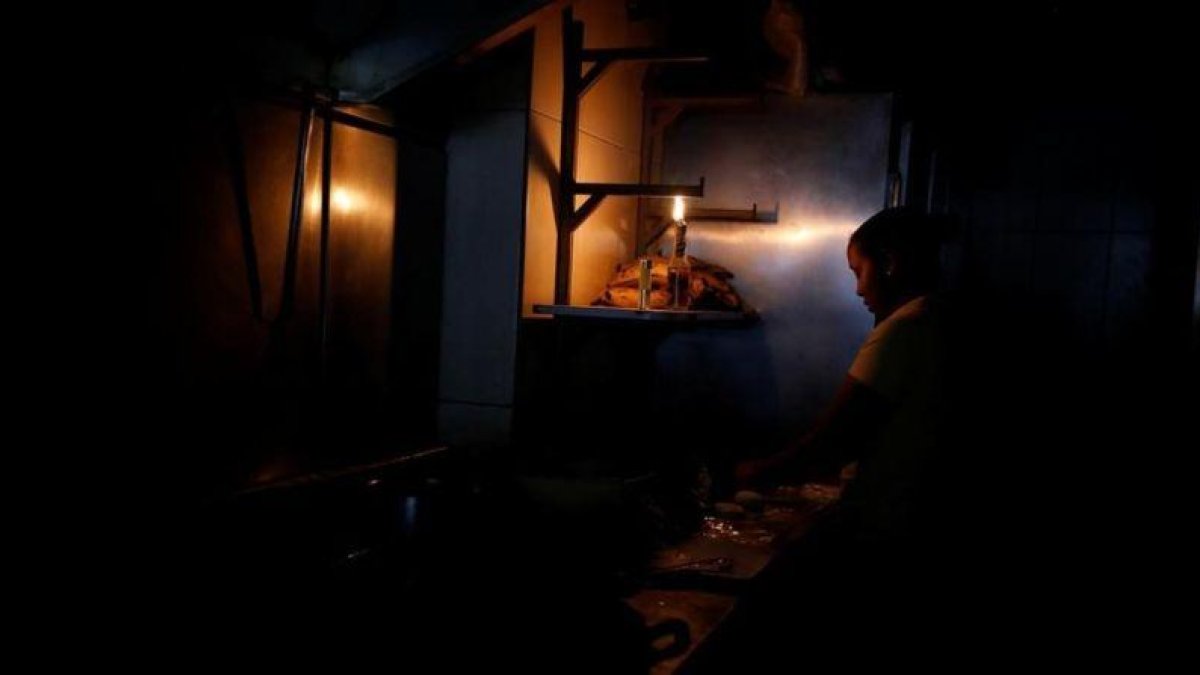 Una mujer usa la luz de una linterna para trabajar en la cocina de un restaurante tras un nuevo apagón en Caracas.