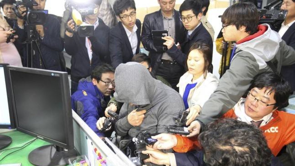 El capitán del 'Sewol', Lee Joon-Seok, con capucha y rodeado de periodistas, en la comisaría de Mokpo, este jueves.