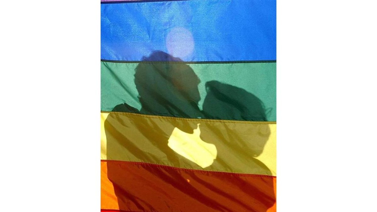 Dos jóvenes se besan tras la bandera LGTBI