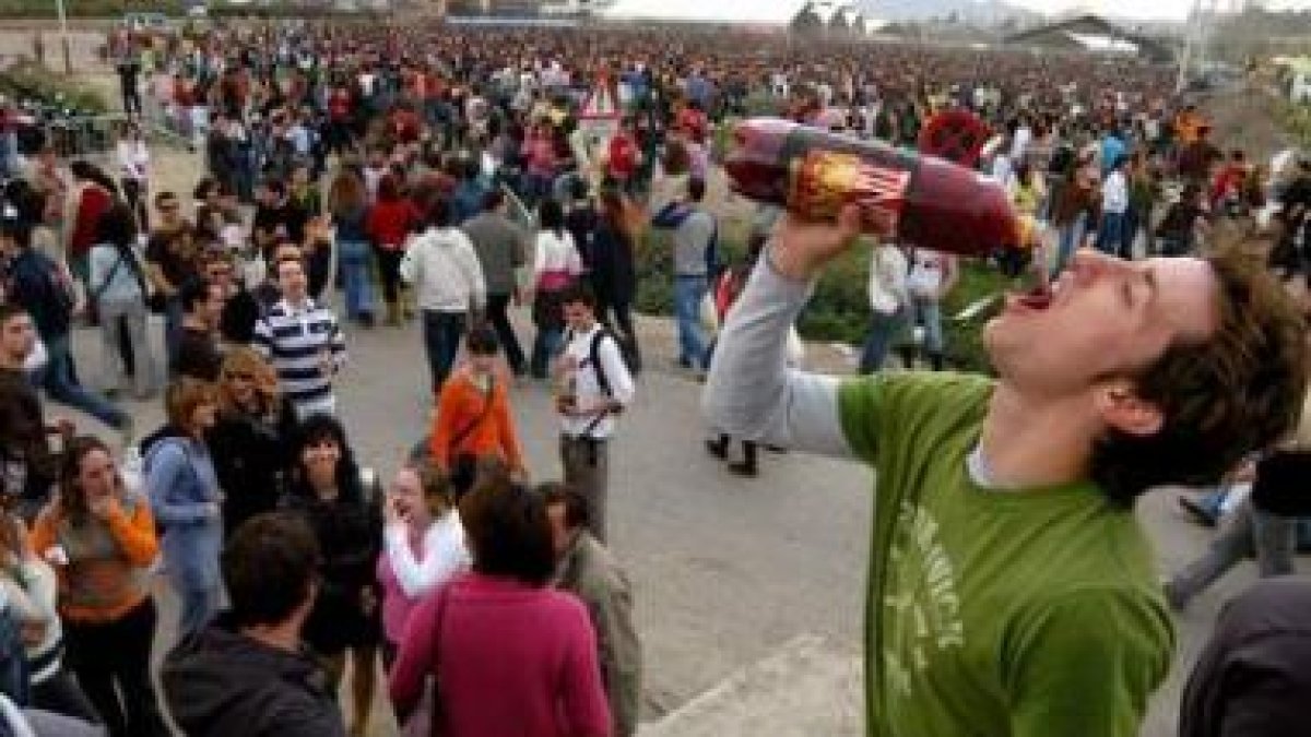 Un joven, en primer término, bebiendo de una botella durante la celebración de un multitudinario bot