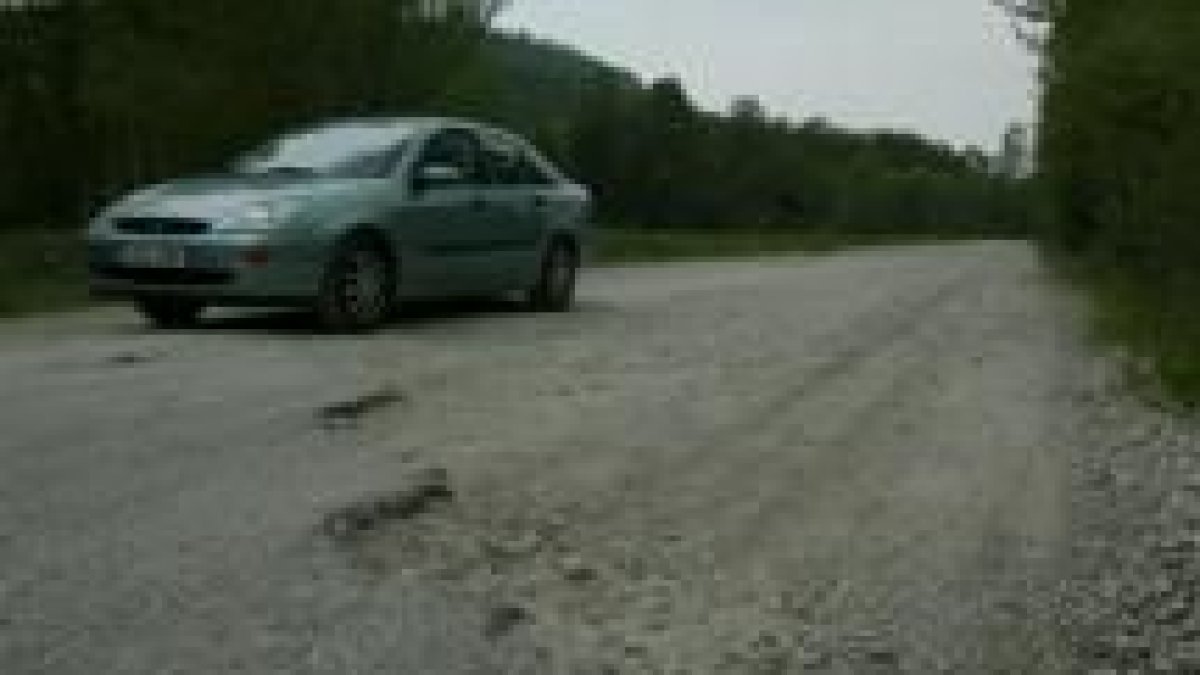 Un vehículo circula por la carretera, donde se pueden ver alguno de los baches