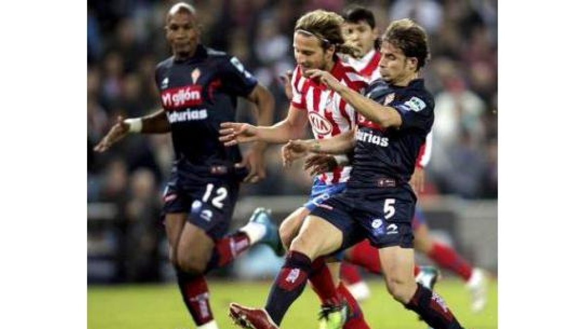 Forlán, que se lesionó, trata de llevarse el balón ante dos jugadores del Sporting de Gijón.