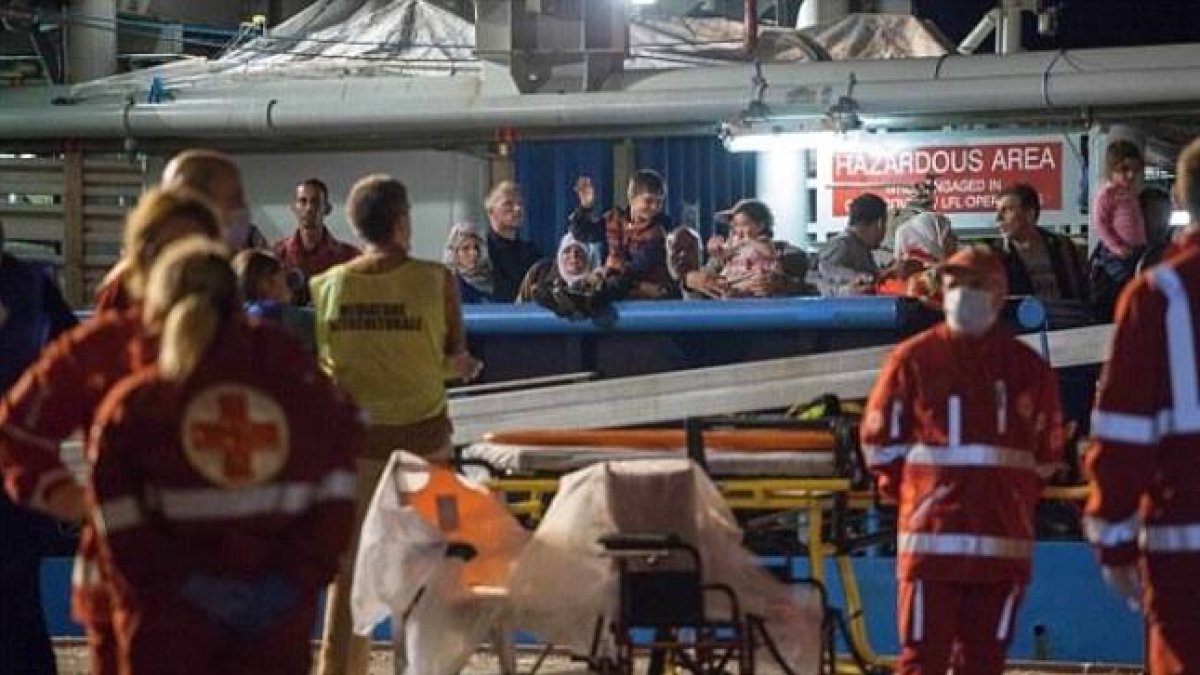 Los inmigrantes supervivientes de un naufragio llegan este jueves a tierra firme tras ser salvados por las autoridades de Libia, mientras los equipos médicos se llevan los cuerpos de los fallecidos.