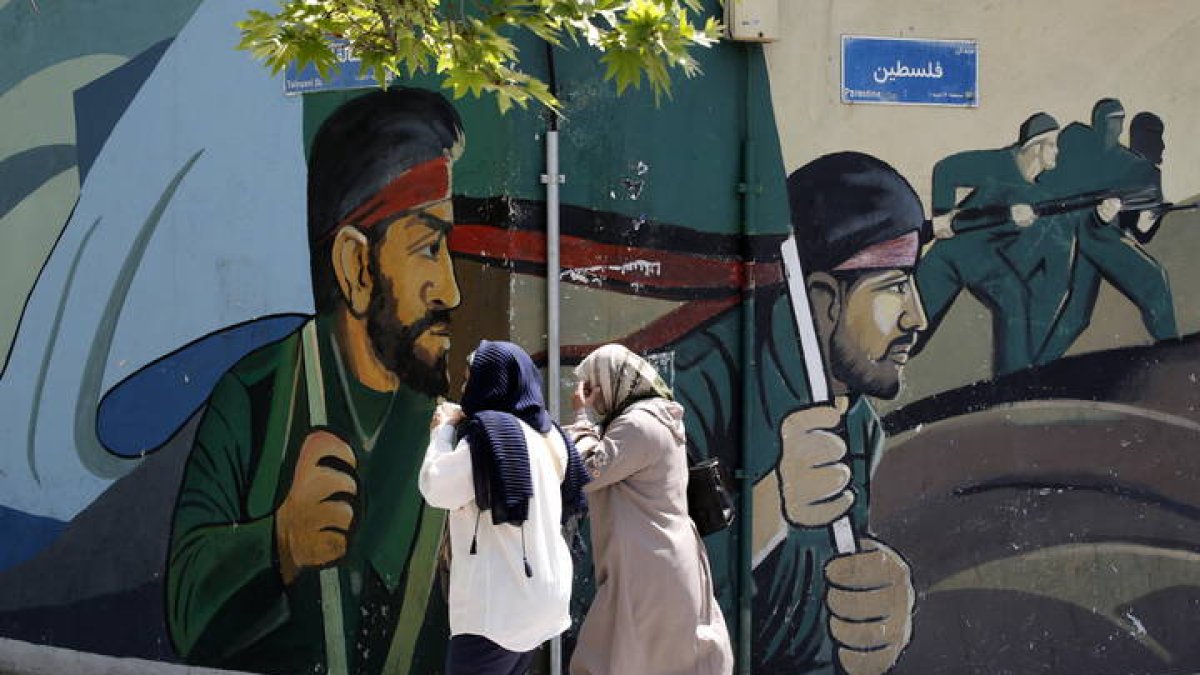 Mujeres iraníes pasan junto a un dibujo callejero de soldados en Teherán.