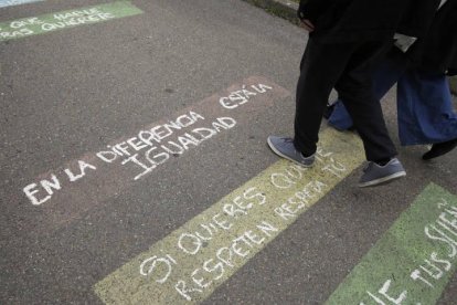 Madre e hijo pasean sobre unos eslóganes pintados frente al colegio de La Virgen.