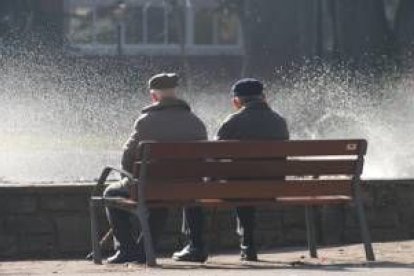 Dos personas mayores descansan en un banco del parque de San Francisco de León