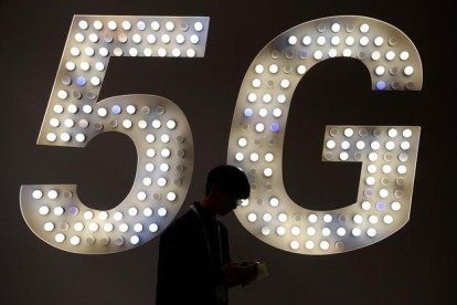 Un visitante usa su teléfono junto a un cartel de 5G en el estand de Intel.