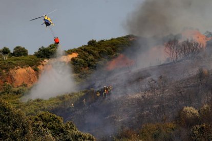 Un helicóptero ataca las llamas desde el cielo mientras las brigadas trabajan en tierra. BARREDO