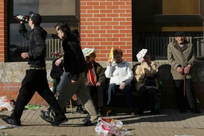 Dos jóvenes pasan bebiendo junto a un grupo de personas mayores.