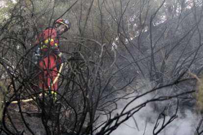 Un miembro de una brigada apaga los rescoldos para evitar que se reproduzca el fuego, en una zona de difícil acceso