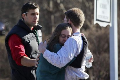 Varias personas se consuelan mutuamente en el exterior de la escuela Sandy Hook.