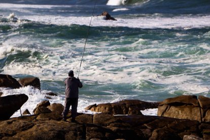 Un pescador lanza su caña sobre el mar picado en la playa de Santa María de Oia (Pontevedra). SALVADOR SAS