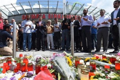 Varias personas rezan en el memorial de velas y flores, colocada frente al centro comercial Olympia, en Munich, este domingo.