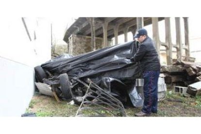 Uno de los vecinos levanta la lona que durante la mañana de ayer cubría el coche destrozado.