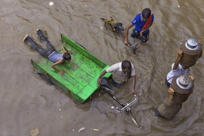 Lecheros intentan abrirse paso por una calle inundada tras las fuertes lluvias en Allahabad, India.  /