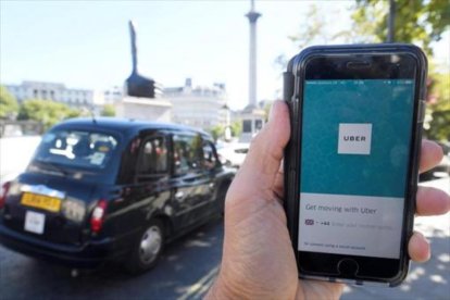 Un taxi de Londres pasa delante de un móvil con la aplicación de Uber activada, ayer.