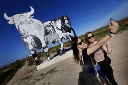 Turistas se acercan a fotografiarse y observar el toro de Osborne que ha aparecido pintado con el escenas del Guernica de Picasso en Santa Pola, Alicante.