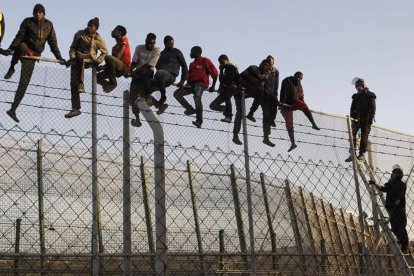 Policías españoles tratan de disuadir a inmigrantes encaramados a la valla de Melilla, fronteriza con Marruecos. /