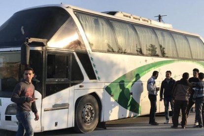 Varias personas permanecen junto a un autobús a la espera de la llegada del resto de evacuados civiles y combatientes.