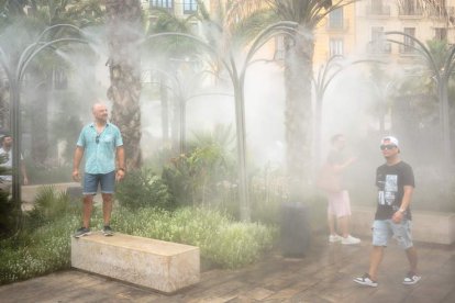 Varias personas se refrescan bajo unos surtidores de agua vaporizada en el centro de Valencia. BIEL ALIÑO