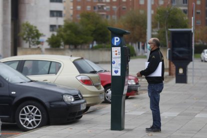 Una persona mete monedas en una máquna de la ORA en León. FERNANDO OTERO