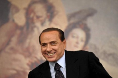 Silvio Berlusconi sonríe mientras toma asiento en una rueda de prensa.