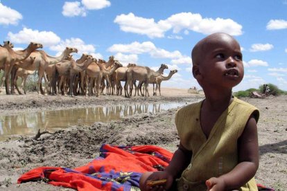 Un niño keniano sentado junto a un charco de agua estancada mientras un grupo de camellos beben en una zona semiárida del norte de Kenia.