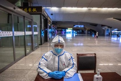 Un operario de trenes con un traje protector espera la llegada de viajeros en Wuhan.