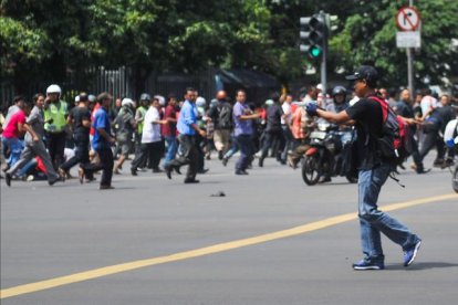 Un hombre armado apunta hacia un centro comercial mientras decenas de personas corren, en el centro de Yakarta.