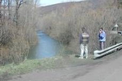 Dos personas observan el lugar concreto de la carretera por el que el vehículo se precipitó al río