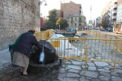 Una mujer coge agua del caño actual; detrás, tapada, la nueva fuente de la plaza.