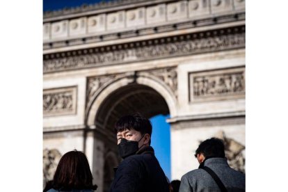 Un turista se protege frente al Arco del Triunfo de París.