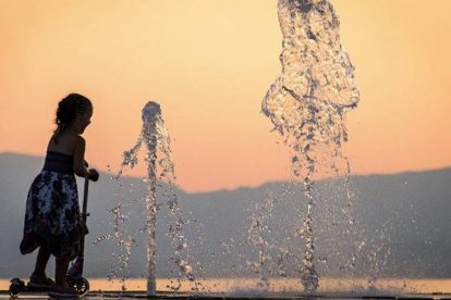 Una niña se refresca en una fuente.