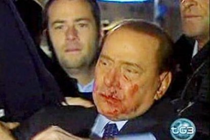 Berlusconi, con la cara ensangrentada, es ayudado por sus escoltas tras la agresión.