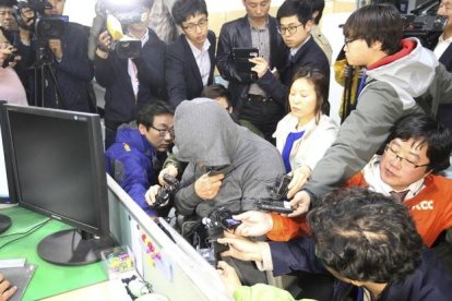 El capitán del 'Sewol', Lee Joon-Seok, con capucha y rodeado de periodistas, en la comisaría de Mokpo, este jueves.