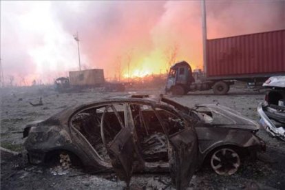 Vista de un coche calcinado en la seria de explosiones de unos almacenes de Tianjin, en China. En segundo plano, el fuego sigue ardiendo.