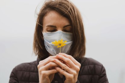 Mujer con mascarilla anti-alérgica observando una flor.