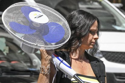 Una mujer lleva un ventilador recién comprado para protegerse del calor.