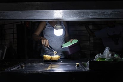 Una persona vende comida ayudado con un bombillo en medio de la oscuridad durante un corte eléctrico, el 29 de febrero de 2024 en Maracaibo (Venezuela). EFE/ Henry Chirinos