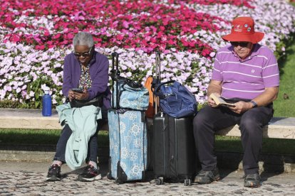 Dos viajeros jubilados descansan en un banco antes de empreder viaje.