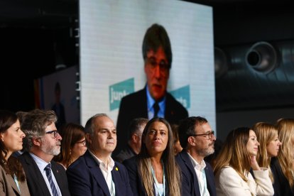 El secretario general de Junts, Jordi Turull (c), escucha la intervención de Carles Puigdemont (en las pantallas) durante el Congreso del partido que se celebra este fin de semana en Calella (Barcelona). EFE/ Quique García