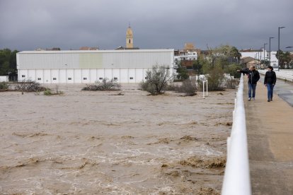 Dos personas contemplan el gran caudal del río Magre a su paso por Alfarp (Valencia) debido a las lluvias torrenciales que afectan a la Comunitat Valenciana, y especialmente a la provincia de Valencia, en la que se ha establecido el aviso rojo. EFE/Ana Escobar