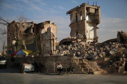 Un vendedor ambulante se sienta el 5 de diciembre de 2024 frente a un edificio dañado mientras la gente se reúne en el lado de la Ciudadela de Alepo (Siria), después de que la oposición tomó control de la ciudad. EFE/EPA/BILAL AL HAMMOUD