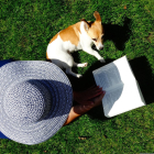 Una mujer lee en una zona verde acompañada de su mascota.