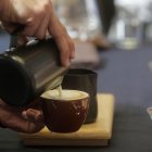 Un camarero sirve un café con leche en un bar.