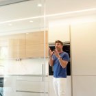 Vista frontal de la cocina reformada por el estudio de Daniel Colino, con materiales como madera y blanco perla y una división en cristal que conecta con el salón.