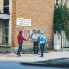 Tres individuos realizan una transacción a plena luz del día, a las puertas de la entrada principal del edificio.