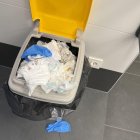 Un contenedor desbordado de pañales y el baño con restos de orina y suciedad en el suelo.