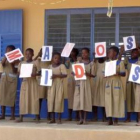 Unos niños africanos muestran carteles formando el nombre de Manos Unidas.